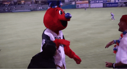 a red mascot with a blue nose is talking to a man