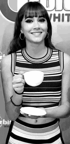 a woman in a striped top is holding a cup of coffee and smiling in a black and white photo .