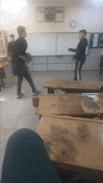 a group of boys are playing basketball in a classroom with a clock on the wall above them