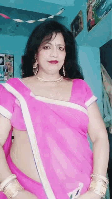 a woman in a pink saree is standing in a room with a blue wall .