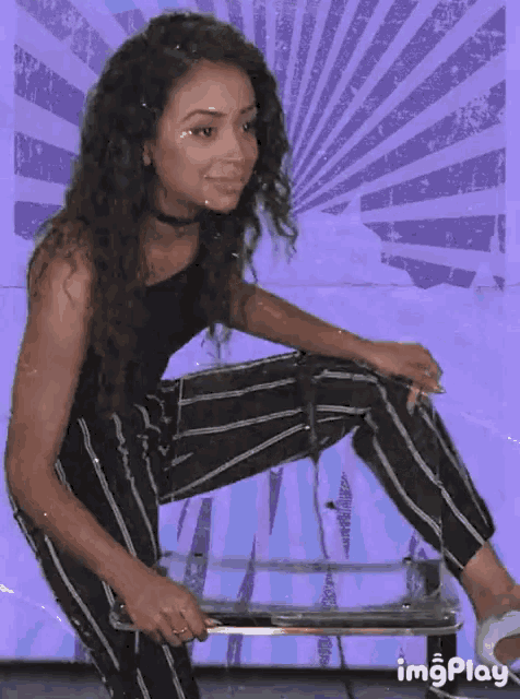 a woman is squatting down with a purple background and the word imgplay is on the bottom right