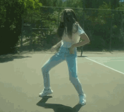 a woman in a white shirt and jeans is dancing on a court