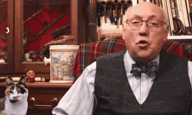 a man wearing glasses and a bow tie is sitting in front of a bookshelf with pipes on it