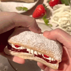 a person is holding a sandwich with powdered sugar and strawberries on it .