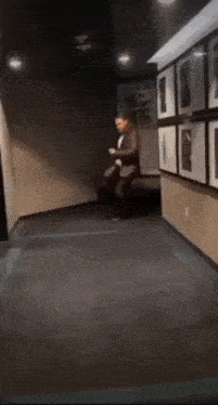 a man in a tuxedo is dancing in a hallway with pictures on the wall