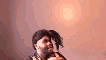 a man wearing a wig and a scarf is standing in front of a pink wall .