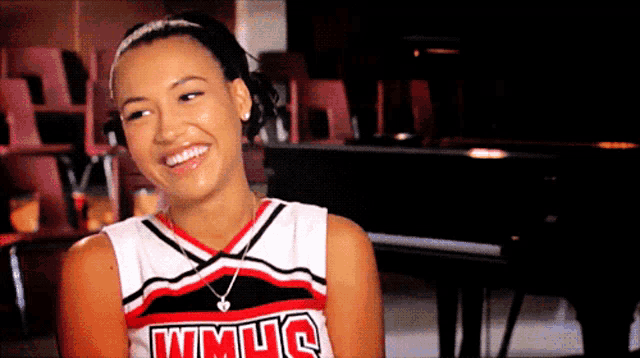 a cheerleader wearing a wmuc uniform smiles while sitting in front of a piano