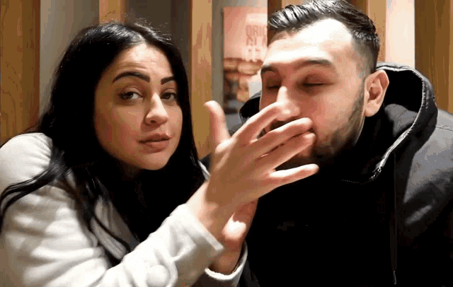a man covering his mouth with his hand while a woman whispers something into his ear