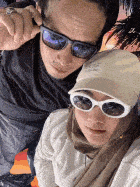 a man wearing sunglasses and a woman wearing a hat with a sticker on it