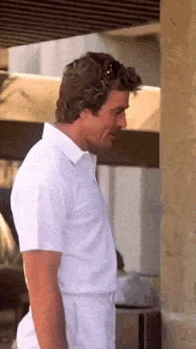 a man in a white shirt and white pants is standing next to a wall .