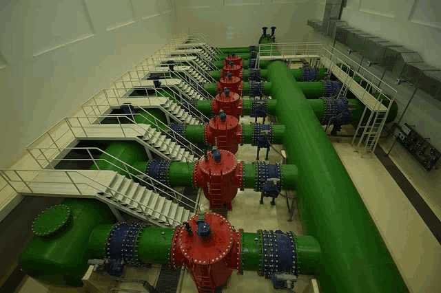 a large room with green pipes and red valves and stairs