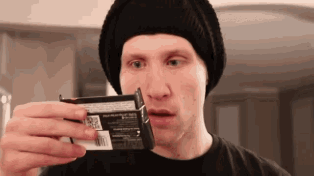 a man wearing a black hat and black shirt is holding a box of cigarettes in his hand