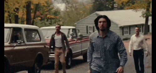 a man in a plaid shirt is walking down a street with other men