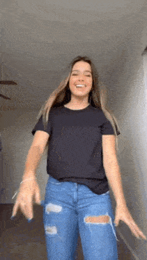 a girl in a black t-shirt and ripped jeans is dancing in a hallway .