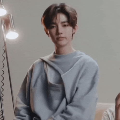 a young man wearing a blue sweater is standing in front of a lamp and looking at the camera .