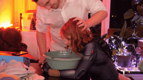 a woman in a black suit sits on a table while a man holds her hair