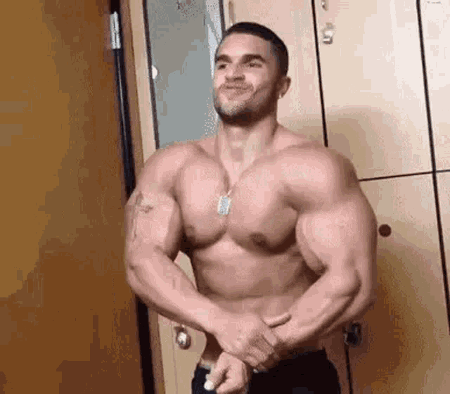 a shirtless man is standing in front of a locker room with his arms crossed .