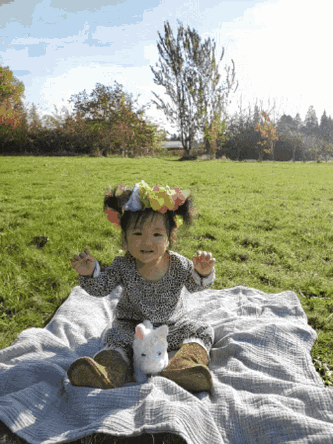 a little girl wearing a flower crown sits on a blanket in the grass