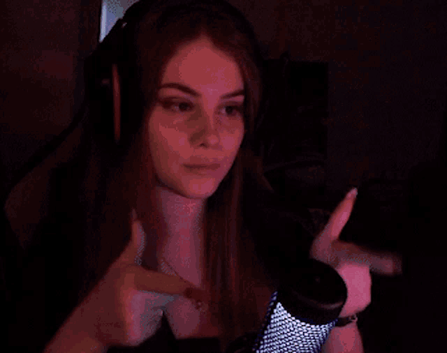 a woman wearing headphones and a necklace is giving a thumbs up sign