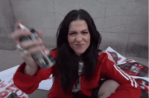 a woman in a red jacket is sitting on the ground holding a can