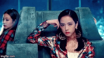 two women are sitting next to each other on a couch . one of the women is wearing a colorful jacket and earrings .