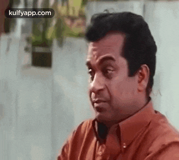 a man in an orange shirt is making a funny face while sitting down .