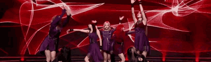 a group of women in purple dresses are dancing on a stage with their arms in the air .
