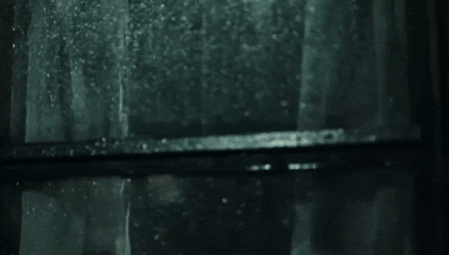 a man with a beard is looking out a window with rain drops on it
