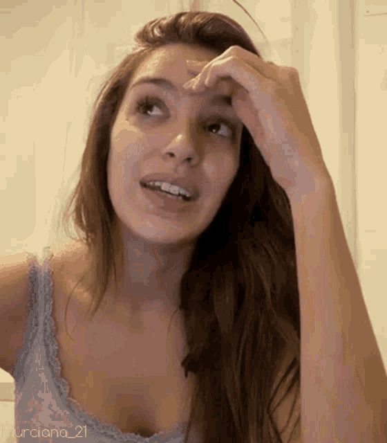 a woman in a blue tank top wipes her nose with her hand