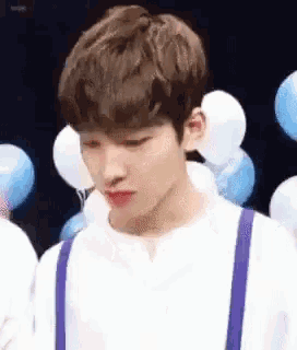 a young man wearing a white shirt and suspenders is standing in front of balloons .
