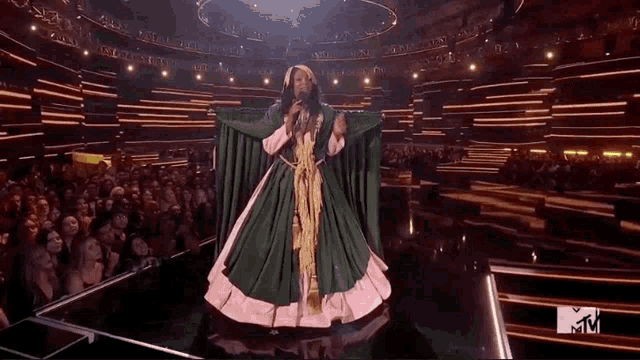 a man in a green and pink dress is singing into a microphone on a stage .