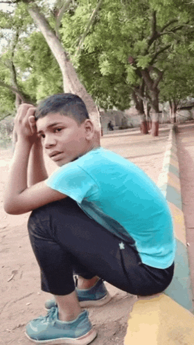 a young boy in a blue shirt is squatting on a curb