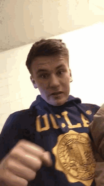 a man wearing a blue ucla sweatshirt is making a face