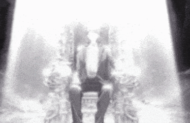 a man in a tuxedo is sitting on a throne in front of a spotlight .