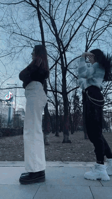 two girls are standing next to each other in a park with trees in the background and a tiktok video of them