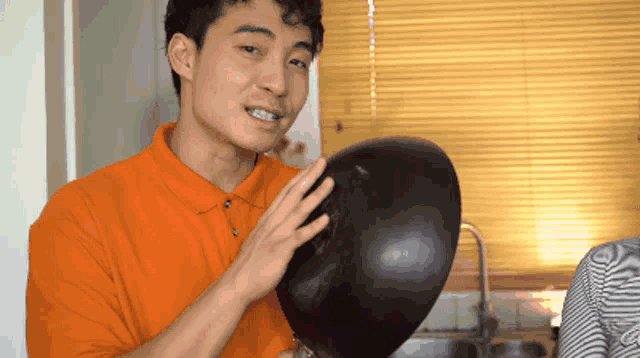 a man in an orange shirt holds a black bowl in his hand