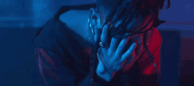 a person is covering their face with their hands in a dark room with blue and red lights .