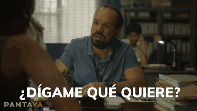 a man sits at a desk with the words " digame que quiere " written on the bottom