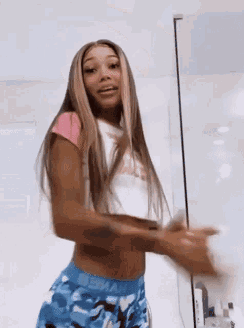 a woman in a pink crop top and blue shorts is standing in a bathroom .