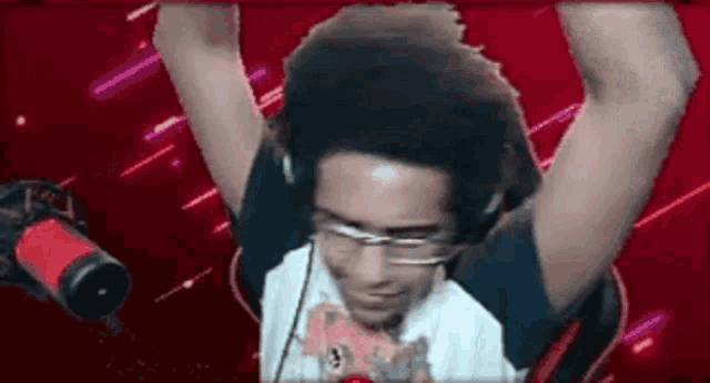 a man wearing headphones and glasses is standing in front of a microphone with his arms in the air .