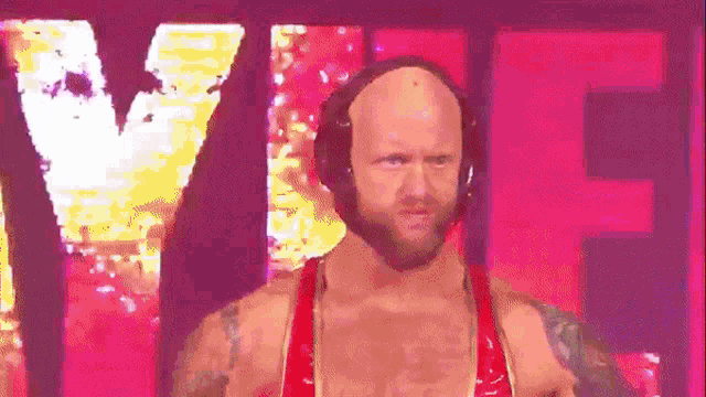 a bald man wearing headphones and a red outfit is standing in front of a large pink sign .