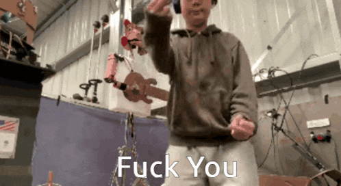 a man wearing headphones and a brown hoodie says fuck you in front of a guitar