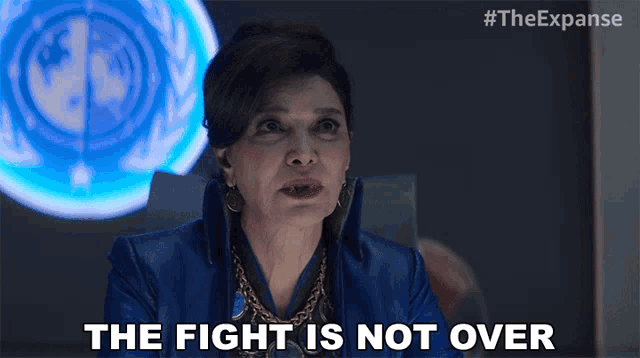 a woman says " the fight is not over " in front of a blue sign