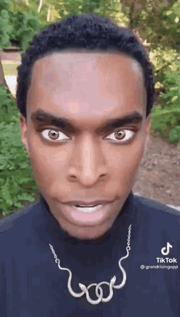 a man wearing a black turtleneck and a necklace with a snake on it is making a funny face .