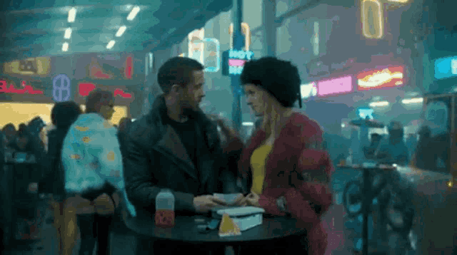 a man and a woman are sitting at a table in front of a sign that says hot