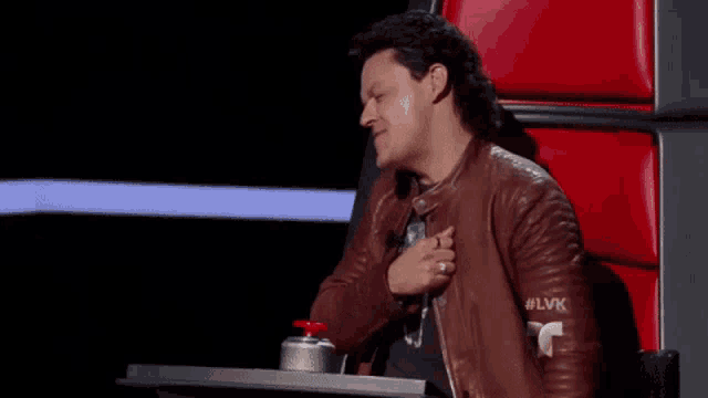 a man wearing a brown leather jacket is sitting at a table with a red button on it .