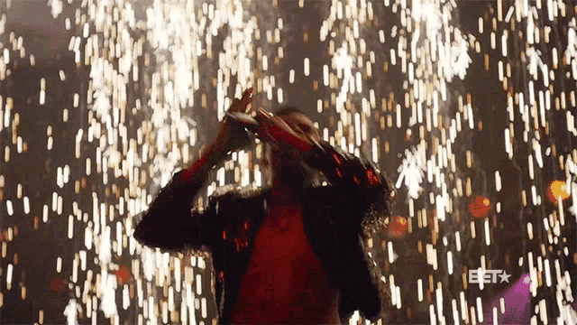 a man in a red shirt stands in front of a fireworks display with the bet logo visible