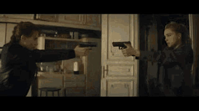 two women are holding guns in a room and pointing at each other .