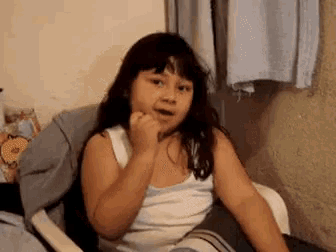 a young girl is sitting in a chair with her hand on her chin .