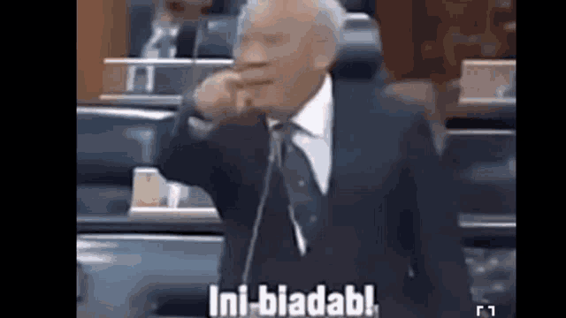 a man in a suit and tie is talking into a microphone and says ini-bladabl